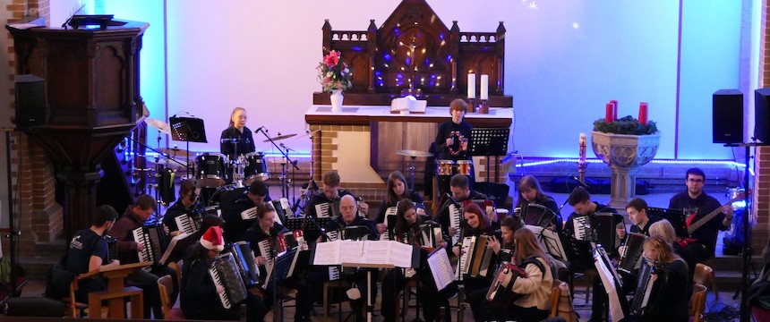 Akkordeonorchester spielt auf der Bühne der weihnachtlich geschmückten Kirche