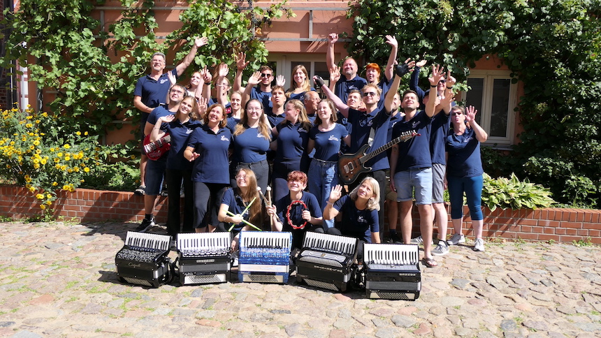Gruppenfoto aller Vereinsmitglieder mit Instrumenten und hochgestrecken Armen