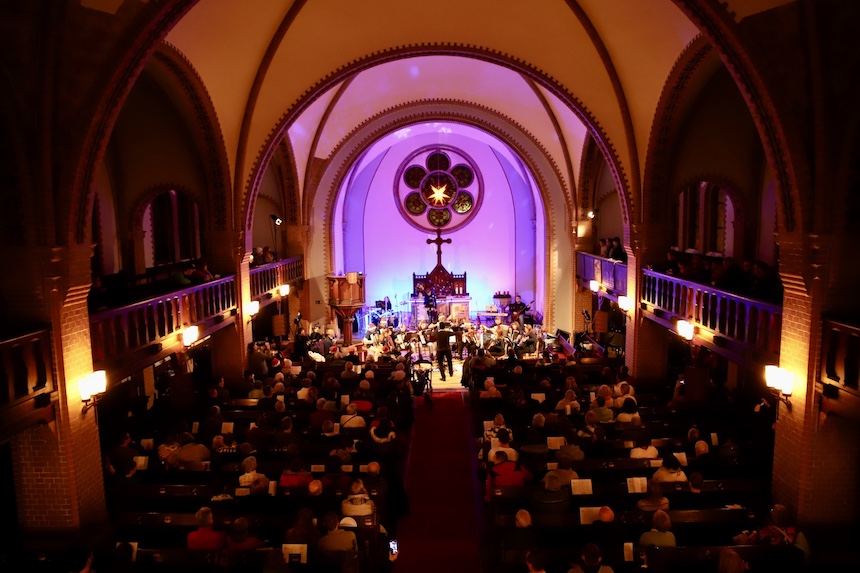 Das Akkordeonorchester auf der bunt beleuchteten Bühne der Kirche, mit Publikum im Vordergrund